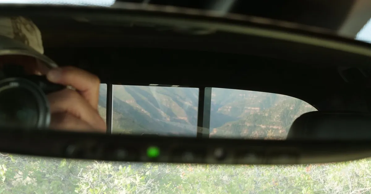 A canyon seen in a truck's rearview mirror, Dave reflected beside it with his camera